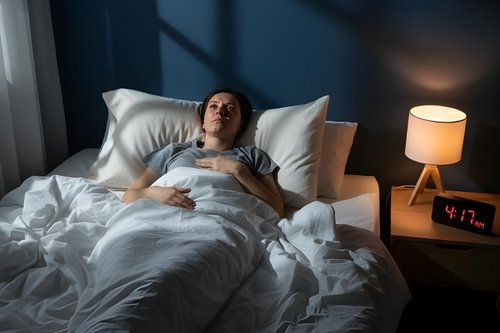 A woman lying awake in bed at 4:17 AM looking for natural drinks for sleep to help her relax.
